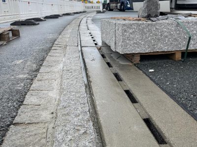 Baustelle mit frisch saniertem Straßenrand, Absperrbaken links, Pflastersteine rechts, LKW im Hintergrund